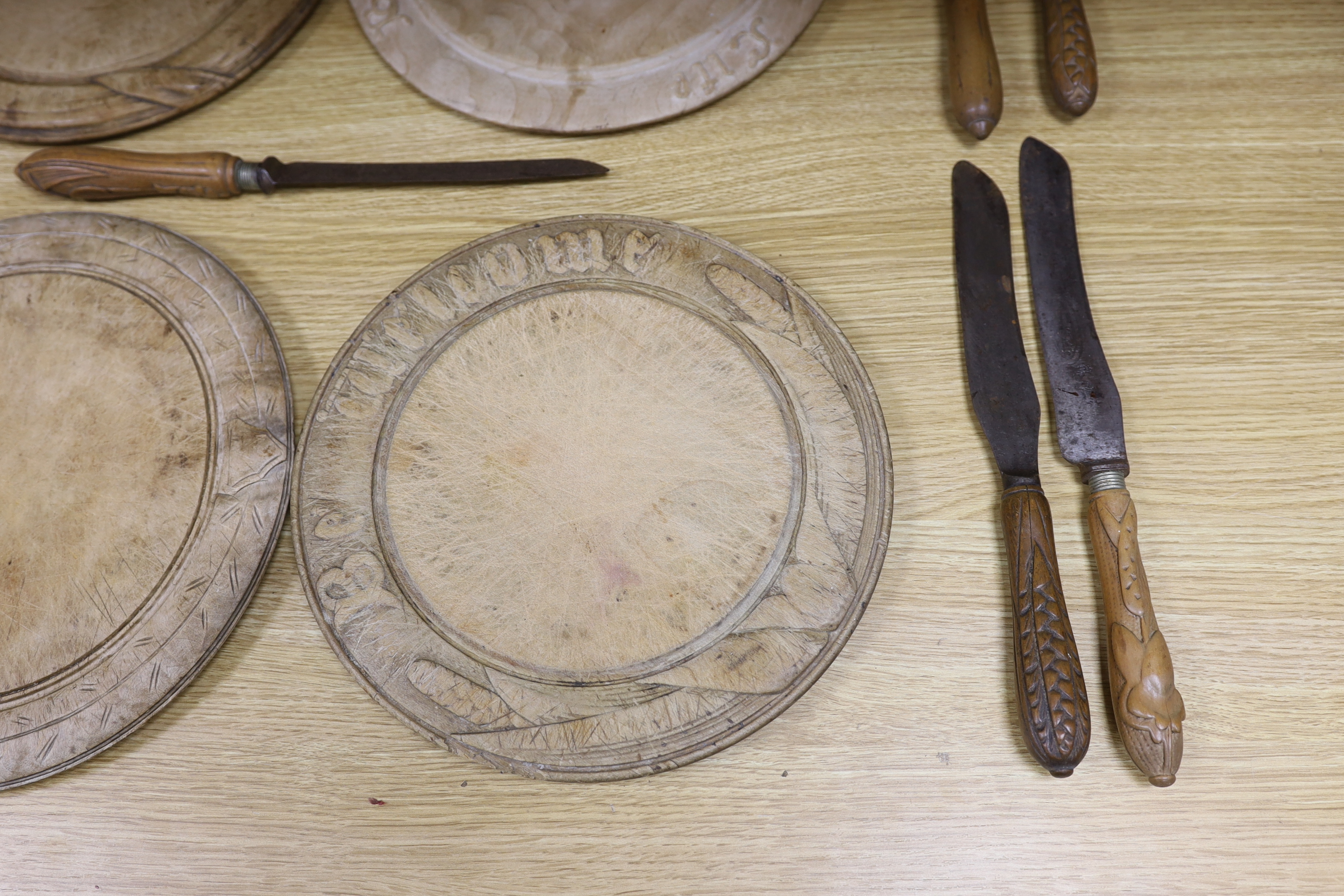 Four carved wood bread boards and a collection of knives with carved handles, boards 28cm in diameter